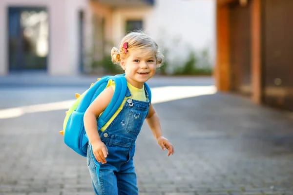 Linda niñita adorable en su primer día yendo a la escuela de juegos. Saludable hermoso bebé caminando a la guardería y jardín de infantes. Niño feliz con mochila en la calle de la ciudad, al aire libre. —  Fotos de Stock