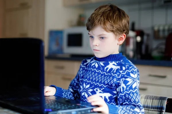 Одинокий мальчик учится дома на ноутбуке для школы. Очаровательный ребенок делает домашнее задание и с помощью ноутбука и современных гаджетов. Концепция домашнего обучения во время карантина пандемического вируса короны — стоковое фото