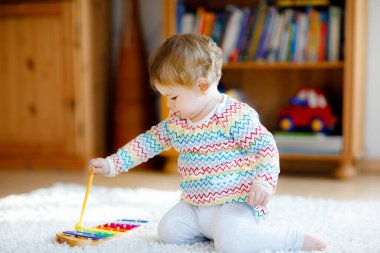 Küçük kız evde ya da çocuk odasında eğitici tahta müzik oyuncaklarıyla oynuyor. Renkli ahşap ksilofonu olan küçük bir çocuk. Korona virüsü salgını sırasındaki yalnız çocuk karantina.