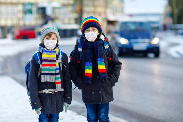 Двоє хлопчиків носять медичну маску на шляху до школи. Діти з рюкзаком. Школярі в холодний зимовий день з теплим одягом. Блокування і карантинний час під час пандемії корона — стокове фото