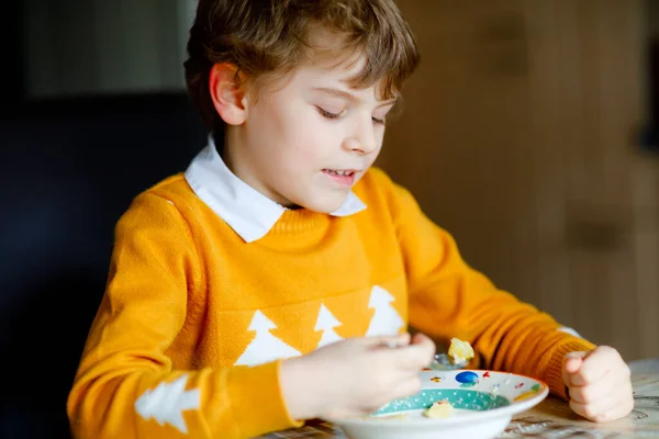 Маленький школьник ест овощной суп. Блондинка на домашней кухне или в школьной столовой. Милый ребенок и здоровая еда, органический веганский суп с лапшой, курицей и овощами. — стоковое фото