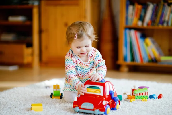 Klein meisje dat thuis of in de kinderkamer met educatief houten speelgoed speelt. Peuter met kleurrijke rode auto. Kind heeft plezier met ander speelgoed. Eenzame jongen tijdens corona virus pandemische quarantaine — Stockfoto