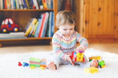 Küçük kız evde ya da çocuk odasında eğitici tahta oyuncaklarla oynuyor. Renkli trenle yürüyen çocuk. Çocuk farklı oyuncaklarla eğleniyor. Korona virüsü salgını sırasındaki yalnız çocuk karantina
