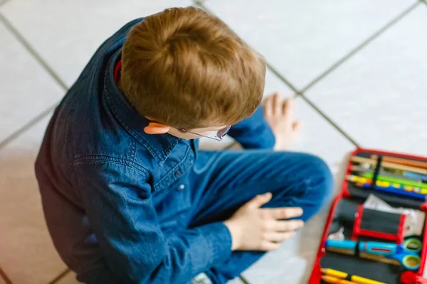 Glücklicher kleiner Schuljunge auf der Suche nach einem Stift im Mäppchen. Gesundes Schulkind mit Brille greift im Grundschulunterricht zu. — Stockfoto