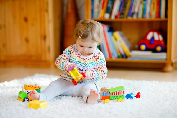 Küçük kız evde ya da çocuk odasında eğitici tahta oyuncaklarla oynuyor. Renkli trenle yürüyen çocuk. Çocuk farklı oyuncaklarla eğleniyor. Korona virüsü salgını sırasındaki yalnız çocuk karantina — Stok fotoğraf