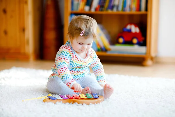 Маленькая девочка играет с образовательными деревянными музыкальными игрушками дома или в детской. Маленький ребенок с красочным деревянным ксилофоном. Одинокий ребенок во время пандемии коронного вируса. — стоковое фото