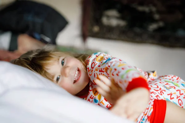 Pequeña niña divirtiéndose en la cama después de despertarse. Un niño sano salta y juega al escondite con los padres. Niño adorable en casa, estilo de vida familiar. —  Fotos de Stock