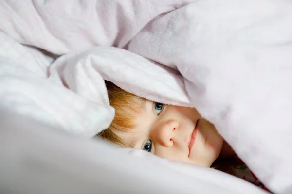 Klein peutermeisje dat plezier heeft in bed nadat ze wakker is geworden. Gezond kind springen en verstoppertje spelen met ouders. Schattig kind thuis, familiale levensstijl. — Stockfoto