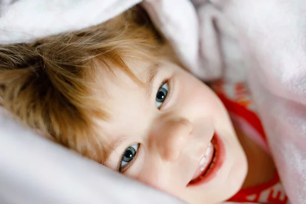 Pequeña niña divirtiéndose en la cama después de despertarse. Un niño sano salta y juega al escondite con los padres. Niño adorable en casa, estilo de vida familiar. — Foto de Stock