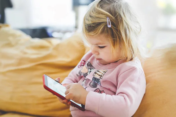 Söt liten flicka leker med smartphone hemma. Friska barnet vidrör telefonen med fingrar, ser tecknade serier och har roligt med pedagogiska spel. Begreppet tidig utveckling — Stockfoto