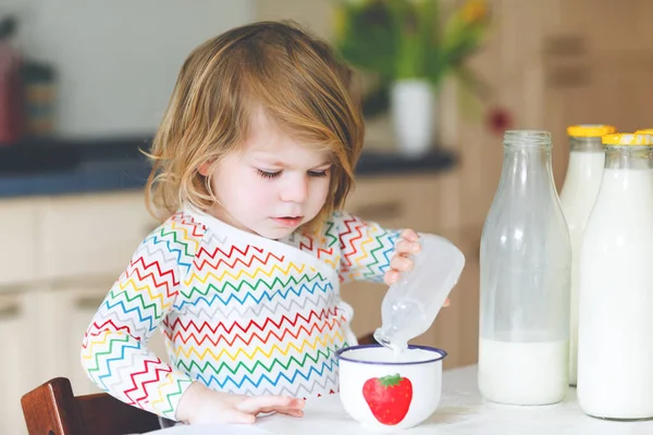 Schattig peutermeisje dat koemelk drinkt als ontbijt. Schattige kleine dochter met veel flessen. Gezond kind dat melk als gezondheidscalciumbron heeft. Kind thuis of in de kinderkamer in de ochtend. — Stockfoto