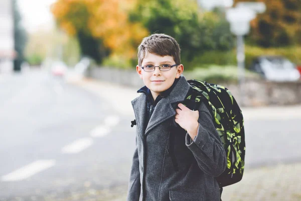 Счастливый мальчик в очках и рюкзаке или сумке. Школьник в стильном фашонском костюме по дороге в среднюю или старшую школу в холодный осенний день. Здоровый ребенок на улице, в дождливый день. — стоковое фото