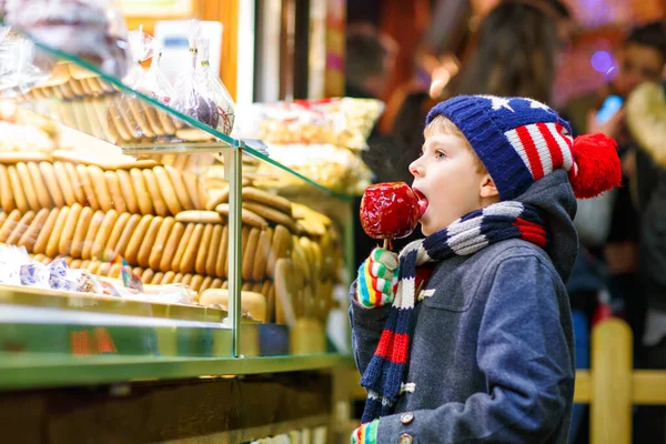 Ευτυχισμένο παιδί που τρώει μήλο καλυμμένο με κόκκινη ζάχαρη στην Χριστουγεννιάτικη αγορά — Φωτογραφία Αρχείου