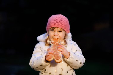 Küçük kız büyük tatlı zencefilli çöreği tutuyor. Komik mutlu çocuk dışarıda sağlıklı ekmek yiyor ve ısırıyor. Aç çocuk..