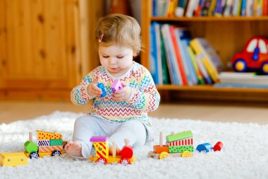 Küçük kız evde ya da çocuk odasında eğitici tahta oyuncaklarla oynuyor. Renkli trenle yürüyen çocuk. Çocuk farklı oyuncaklarla eğleniyor. Korona virüsü salgını sırasındaki yalnız çocuk karantina