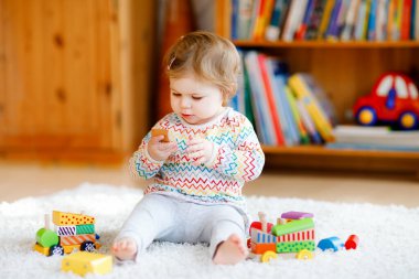 Küçük kız evde ya da çocuk odasında eğitici tahta oyuncaklarla oynuyor. Renkli trenle yürüyen çocuk. Çocuk farklı oyuncaklarla eğleniyor. Korona virüsü salgını sırasındaki yalnız çocuk karantina