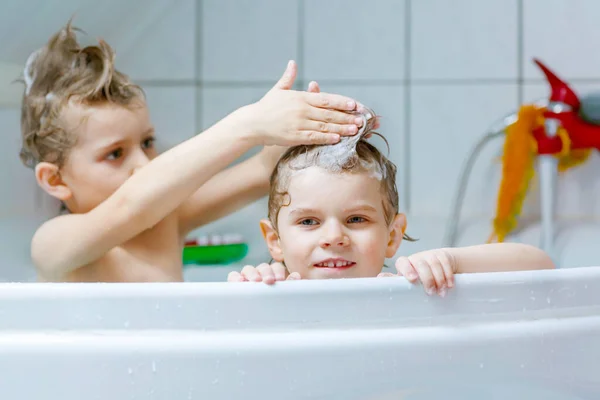 Happy broertjes en zusjes: Twee kleine gezonde tweelingen spelen samen met water door thuis in bad te gaan. Jongetjes die plezier hebben samen. kinderen wassen hoofden en haren met shampoo. — Stockfoto