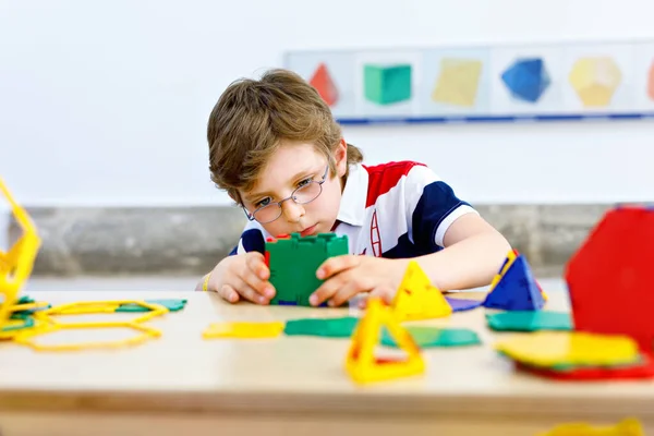 Happy kid boy with glasses having fun with building and creating geometric figures, learning mathematics and geometry — Stock Photo, Image