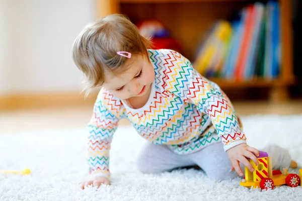 Κοριτσάκι που παίζει με εκπαιδευτικά ξύλινα παιχνίδια στο σπίτι ή το νηπιαγωγείο. Παιδί με πολύχρωμο τρένο. Το παιδί διασκεδάζει με διαφορετικά παιχνίδια. Μοναχικό παιδί κατά τη διάρκεια της πανδημικής καραντίνας του ιού — Φωτογραφία Αρχείου