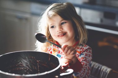 Çikolata hamuru yiyen tatlı bir kız kaşıkla dinleniyor ve ottan parmakları çıkıyor. Mutlu çocuk kek ya da kek için tatlı hamuru yalıyor, evde mutfağa ve eve yardım ediyor..