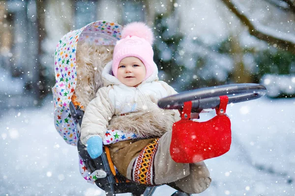 Söt liten vacker liten flicka sitter i barnvagn eller barnvagn på kall snöig vinterdag. Glad leende barn i varma kläder, mode snygg baby coat. Babys första snö. — Stockfoto