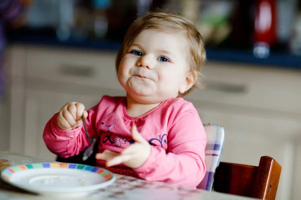 Niña feliz comiendo croissant fresco para el desayuno o el almuerzo. Alimentación saludable para los niños. Niño pequeño en pijama colorido sentado en la cocina doméstica después de dormir en la mañana — Foto de Stock