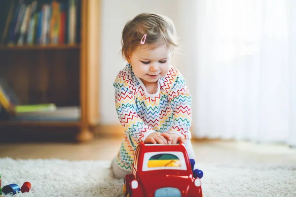 小女孩在家里或托儿所玩教育用的木制玩具。带着五彩缤纷的红色轿车的小孩儿。孩子们玩不同的玩具。在科罗纳病毒大流行检疫期间孤独的孩子 — 图库照片