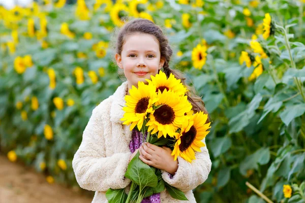 Schattig schoolmeisje op zonnebloemenveld met gele bloemen. Mooi kleuter met blond haar. Gelukkig gezond dochtertje, glimlachend en boeket vasthoudend — Stockfoto