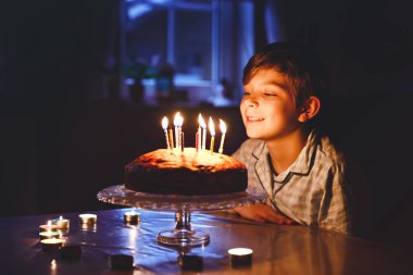 Sevimli, mutlu, küçük sarışın çocuk doğum gününü kutluyor. Çocuk ev yapımı kek üzerine mum üflüyor, kapalı alanda. Okul çocukları için doğum günü partisi, aile kutlaması