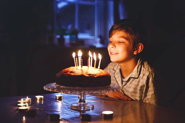 Imádnivaló szőke kisfiú, aki a születésnapját ünnepli. Gyertyákat fúj házi süteményre, beltérben. Születésnapi party iskolásoknak, családi ünnep — Stock Fotó