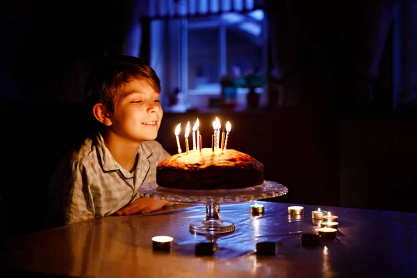 Uroczy blondyn świętujący urodziny. Dziecko dmucha świeczki na domowej roboty torcie, wewnątrz. Przyjęcie urodzinowe dla dzieci w wieku szkolnym, uroczystość rodzinna — Zdjęcie stockowe