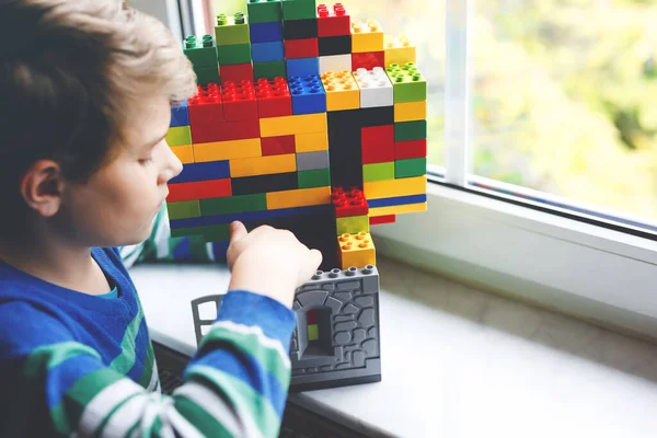 Menino brincando com muitos blocos de plástico coloridos. Criança adorável da escola se divertindo com a construção e criação de construção por janela. Técnico de lazer criativo e robótico durante o tempo corona — Fotografia de Stock