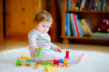 Küçük kız evde ya da çocuk odasında eğitici tahta oyuncaklarla oynuyor. Renkli trenle yürüyen çocuk. Çocuk farklı oyuncaklarla eğleniyor. Korona virüsü salgını sırasındaki yalnız çocuk karantina