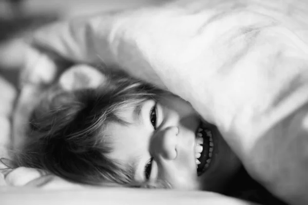 Pequeña niña divirtiéndose en la cama después de despertarse. Un niño sano salta y juega al escondite con los padres. Niño adorable en casa, estilo de vida familiar. — Foto de Stock