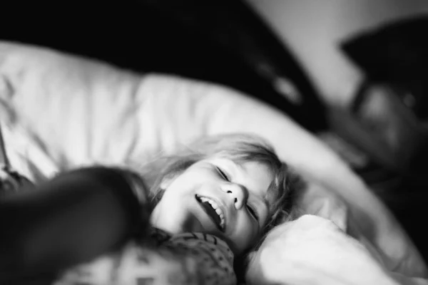 Kleines Mädchen, das nach dem Aufwachen Spaß im Bett hat. Gesunde Kinder springen und spielen mit ihren Eltern Verstecken. Liebenswertes Kind zu Hause, Familienleben. — Stockfoto