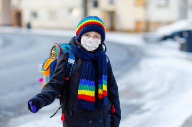 Okula giderken gözlüklü, tıbbi maske takan küçük çocuk. Çocuk sırt çantası çantası. Kış günü okul çocuğu kalın giysilerle. Corona salgını sırasında tecrit ve karantina süresi