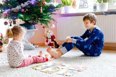 İki küçük çocuk, küçük tatlı kız ve okul çocuğu süslü Noel ağacında kağıt oynuyorlar. Mutlu sağlıklı kardeşler, erkek ve kız kardeşler birlikte eğleniyor. Aile Xmas kutlaması