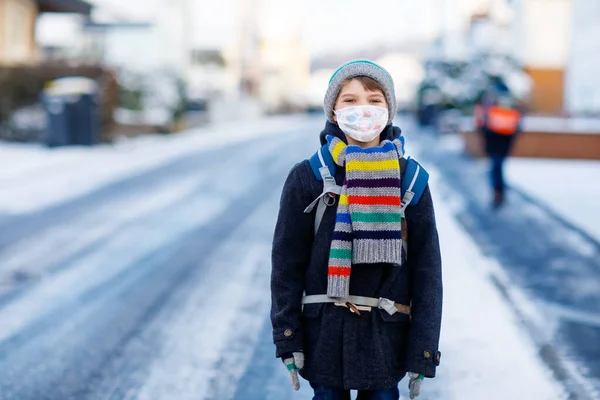 Little kid boy with glasses wearing medical mask on the way to school. Child backpack satchel. Schoolkid on winter day with warm clothes. Lockdown and quarantine time during corona pandemic disease — Stock Photo, Image