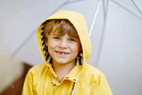 Bellissimo bambino sulla strada per la scuola a piedi durante sleet, pioggia forte e neve con un ombrello nella giornata fredda. Bambino felice e gioioso in abiti casual colorati cappotto giallo moda — Foto Stock