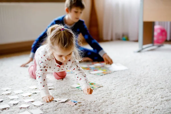 Два маленьких ребенка, симпатичная девочка и школьник играют вместе в карточную игру у украшенной елки. Счастливые здоровые братья и сестры, веселятся вместе. Семья празднует Рождество — стоковое фото