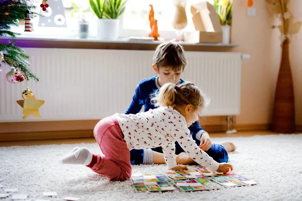 Två små barnsliga, söta småbarn flicka och skolpojke leker tillsammans kortspel av dekorerad julgran. Glada friska syskon, bror och syster ha kul tillsammans. Familjen firar jul — Stockfoto