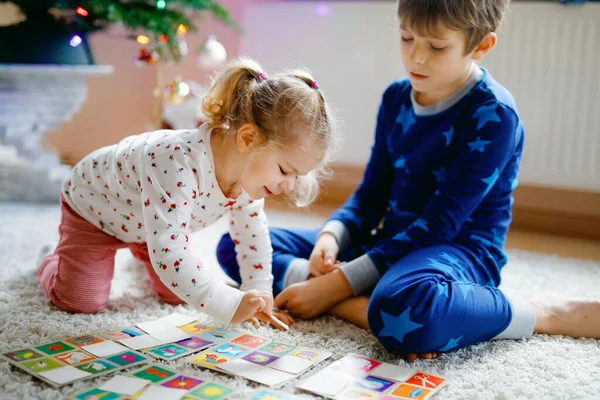 Två små barnsliga, söta småbarn flicka och skolpojke leker tillsammans kortspel av dekorerad julgran. Glada friska syskon, bror och syster ha kul tillsammans. Familjen firar jul — Stockfoto