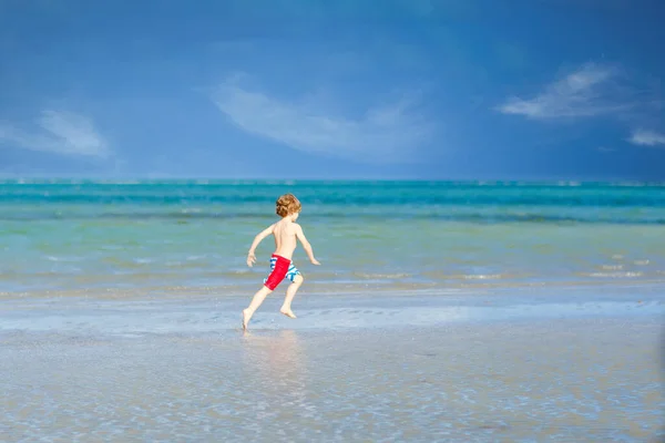 Niño activo divirtiéndose en la playa de Miami, Key Biscayne. Feliz niño lindo corriendo cerca del océano en un día cálido y soleado. Niño sano en pantalones de baño cazando aves gaviotas — Foto de Stock