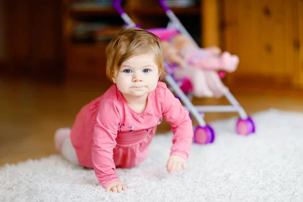 Aranyos aranyos kislány mászik és babakocsival játszik. Gyönyörű kisgyermek toló babakocsi játékkal otthon. Boldog gyerek két babával. — Stock Fotó