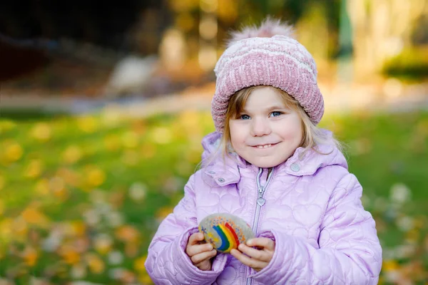 Adorabile bambina con arcobaleno dipinto su pietra durante la quarantena del coronavirus pandemico, all'aperto. Bambino pittura arcobaleni in tutto il mondo come speranza, segno e lotta contro il virus covid corona — Foto Stock