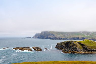 Malin Head, Donegal, İrlanda 'da engebeli bir manzara. Kayalıklı sahil, sisli bulutlu bir günde koyunlu yeşil kayalık arazi. Vahşi Atlantik Yolu bölgesi.