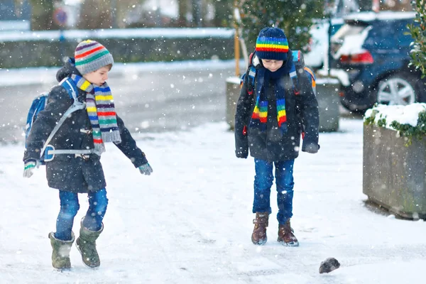 下大雪时，两个小学的小男孩步行去学校。快乐的孩子们玩的开心，玩的是初雪。姐姐们的朋友们，背着五颜六色的冬衣背包. — 图库照片