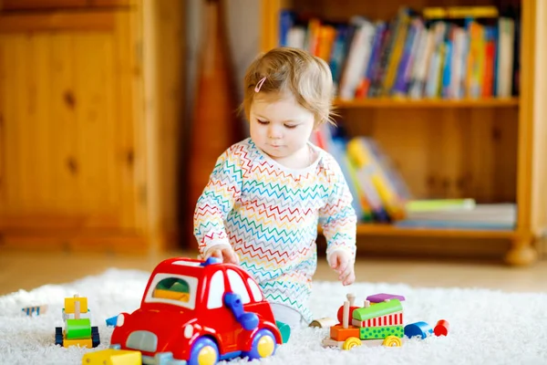 Pequena menina brincando com brinquedos educativos de madeira em casa ou no berçário. Criança com carro vermelho colorido. Criança se divertindo com brinquedos diferentes. Criança solitária durante quarentena pandêmica do vírus da corona — Fotografia de Stock