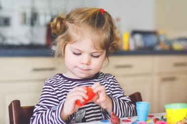 Renkli killi, sevimli, küçük bir kız. Sağlıklı bebek oyun oynuyor ve oyun hamurundan oyuncaklar yapıyor. Küçük çocuk kil kalıp ve öğrenim