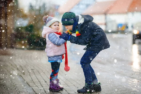 Okul çocuğu ve erkek kardeşi soğuk, karlı kış gününde küçük kız ve kız kardeşinin ellerini ısıtıyorlar. Aile, iki sevimli kardeş karla oynayan çocuklar, kar yağarken dışarıda.. — Stok fotoğraf